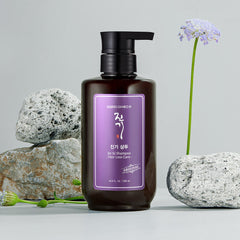 Brown shampoo bottle with purple label on a gray background with rocks and flowers