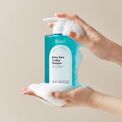 Hand holding a bottle of Daeleaf Better Root Cooling Shampoo with foamy texture against a beige background
