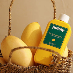 Yellow bottle of Julioly hair product with mangoes in a woven basket on a beige background