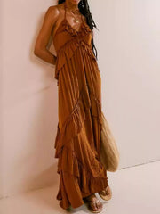 A woman wearing a long, tiered maxi dress in a warm rust brown color, standing against a plain off-white wall.